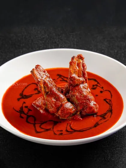 Chaap in a spicy red gravy, presented with a modern fine-dining aesthetic.