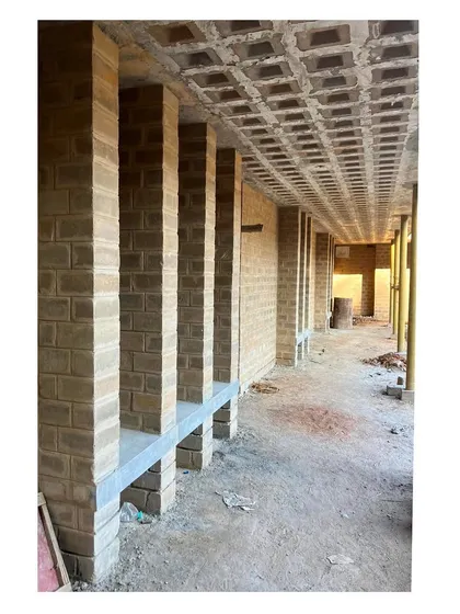 A view of the corridor under construction, showing the exposed brick pillars and the coffered detail of the filler slab ceiling. This highlights the structural honesty of the design.