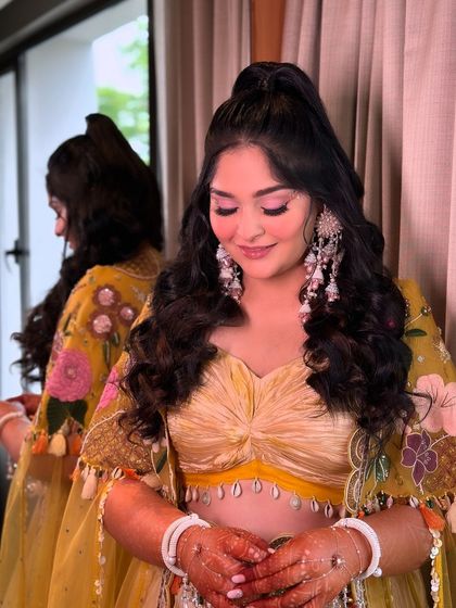 A chic half-up ponytail with voluminous curls, perfect for a Haldi or daytime event. This style keeps hair away from the face while still showing off its length and texture.