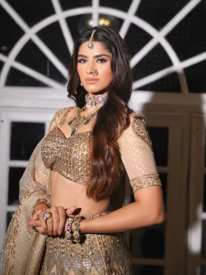 A three-quarter view of the golden lehenga. The styling showcases the beautiful details on the sleeves and the matching jewelry.