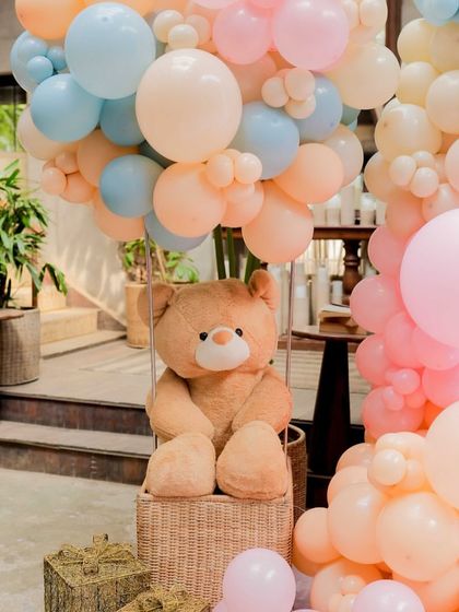 It's all in the details. This close-up shows a cuddly teddy bear ready for adventure in a wicker hot air balloon basket, a charming element from our 'Up, Up & Away' baby shower decor.