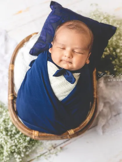 This little gentleman is ready for his dreams. A newborn swaddled in a deep blue wrap with a matching pillow and bow tie makes for a truly charming portrait.
