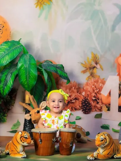 This little jungle explorer is celebrating her first birthday by playing the bongo drums, surrounded by animal friends.