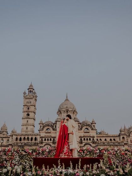 An epic wide shot of the couple on a stage in front of the entire Laxmi Vilas Palace.