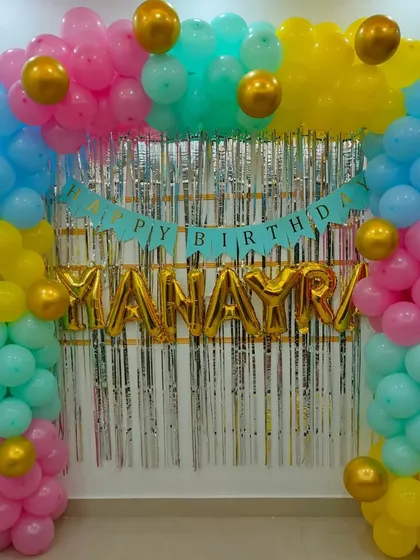A simple and colorful balloon arch with a silver shimmer curtain and a 'Happy Birthday' banner, perfect for a vibrant home party.