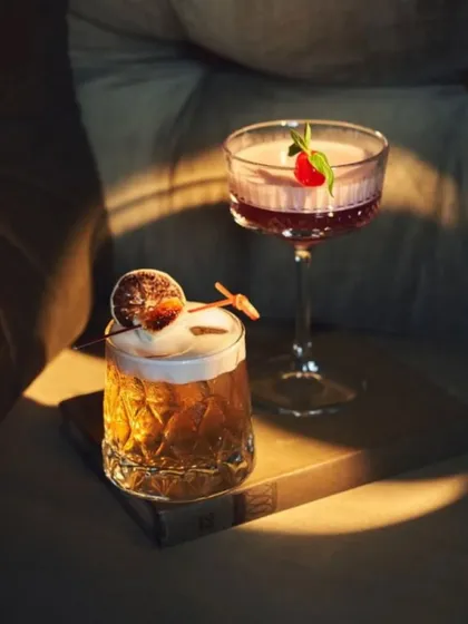 Two of our signature cocktails, a whiskey sour and a clover club, resting in a spot of sunlight, showcasing their beautiful colors and garnishes.