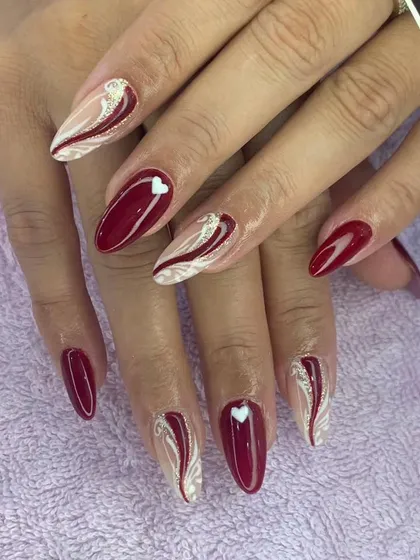 A romantic design with deep red polish and accent nails featuring white swirls and a tiny heart.
