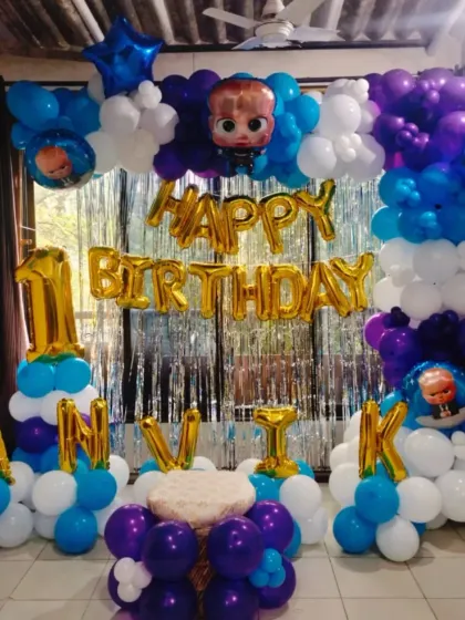 A fun "Boss Baby" themed first birthday party. The decoration includes character cutouts, blue, purple, and white balloons, and foil letters spelling out the birthday boy's name.