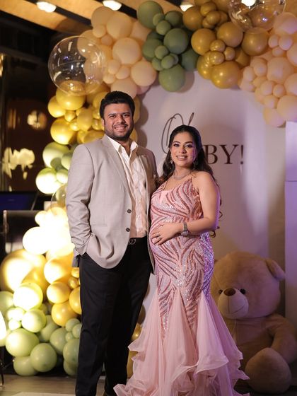 The happy couple posing together at their green and gold teddy bear themed baby shower. The balloon arch provides a perfect frame for their memorable photos.