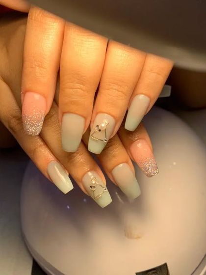 A soft, muted green set with glittery tips and delicate triangular gold charms.