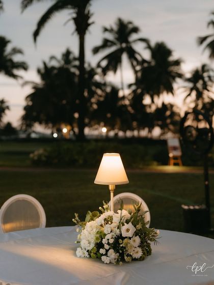 A table centerpiece with a lamp, set against the backdrop of palm trees and the evening sky.