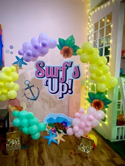 Surf's up for a fun beach-themed party! The decor includes a custom "Surf's Up!" sign, starfish, and colorful balloons to create a tropical vibe.