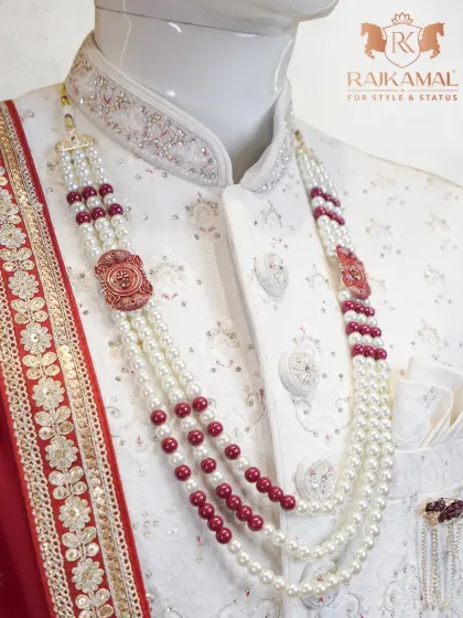 A close-up of a groom's necklace, featuring layers of pearls and red beads, perfectly complementing the white sherwani.