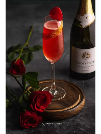 A romantic red wine cocktail garnished with a rose petal, shot for Whiskey Amour. The composition with fresh roses adds to the story, making it perfect for a Valentine's or special occasion menu.