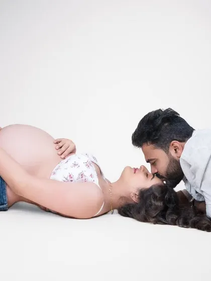 A simple, pure, and intimate moment. Lying on the clean white studio floor, the focus is entirely on their connection. His gentle kiss and her peaceful expression tell a story of complete trust and love.