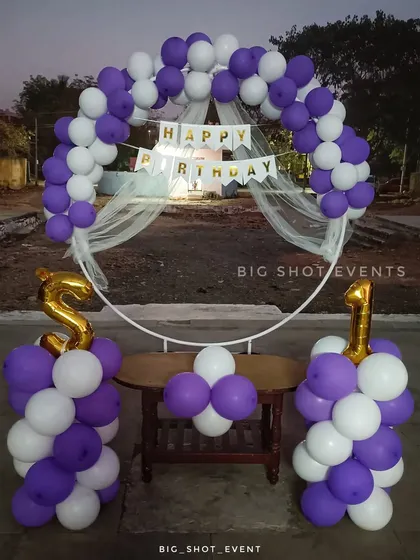 A simple and budget-friendly first birthday decoration for an outdoor space, using a circular frame with purple and white balloons and foil number balloons.