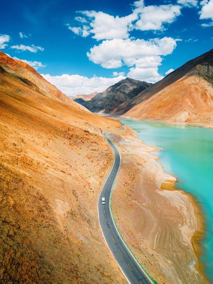 A road that feels like a highway to heaven. This drone shot captures a lone car on a winding road next to a brilliant turquoise lake in Tibet, showcasing the epic scale and beauty of the region.