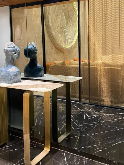 A close-up of a console table arrangement. This detail shot highlights the contrast between the black marble floor, the brushed gold legs of the table, and the sculptural art pieces, showcasing our focus on material and form.
