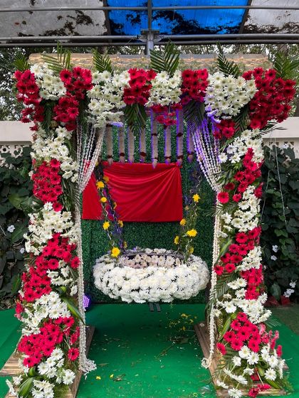 A beautiful cradle for a naming ceremony, fully decorated with red and white flowers. The simple green backdrop ensures that the ornate cradle remains the main focus.