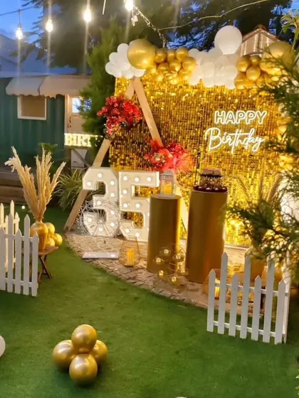 A glamorous 35th birthday party setup featuring a gold sequin wall. The decor is enhanced with marquee numbers, a neon sign, and a gold and white balloon arrangement, perfect for an evening celebration.