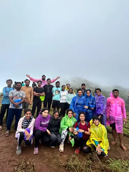 A large group at a foggy viewpoint. The mist adds a layer of mystery and beauty to the trekking experience in the ghats, making for dramatic photos.