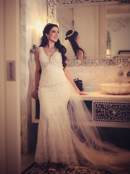 A full-length shot of a bride in a beautiful white lace wedding dress, posing in an elegant bathroom.