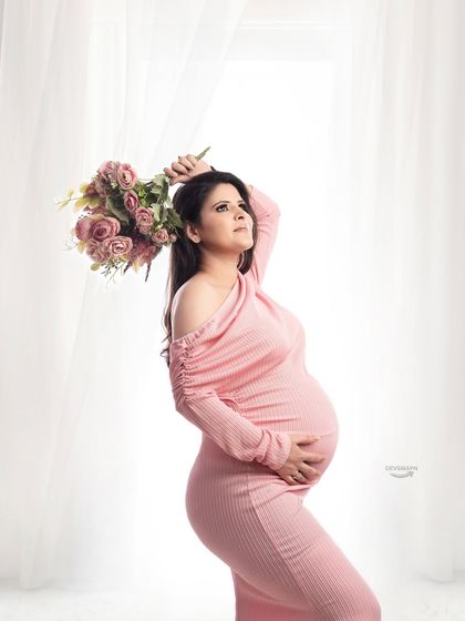 An elegant pose with a bouquet of flowers, adding a touch of romance to the portrait. The fitted pink gown and bright background create a fresh and beautiful maternity image.