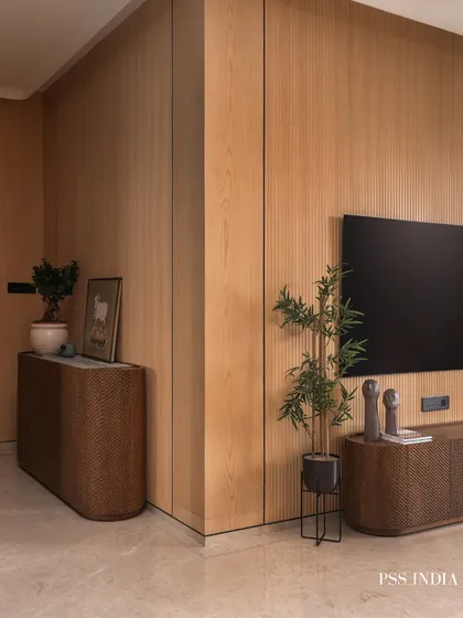 A view of a modern living room corner, where fluted oak wall panels meet a textured media console. The addition of plants brings life and a natural element to the clean, architectural lines.