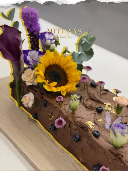 This 6kg decadent chocolate log cake was created for a baby shower, designed to feel like a piece of an enchanted forest. It's decorated with fresh blueberries, edible butterflies, and a beautiful arrangement of fresh, seasonal flowers.