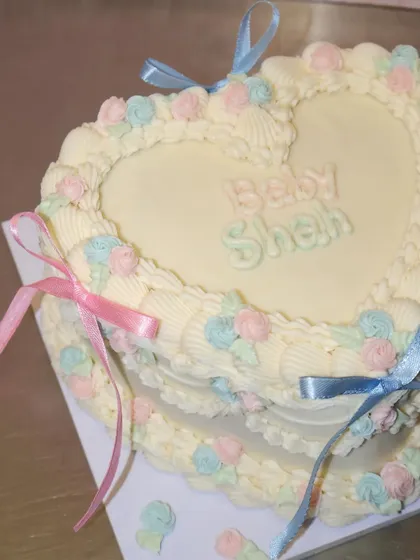 A sweet little cake for a sweet little baby. This heart-shaped baby shower cake features pastel pink and blue buttercream roses and matching ribbons.