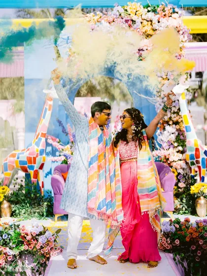 A blast of color! Laxmi and Roshan are framed by yellow and blue smoke, creating a dynamic and unforgettable image from their Haldi celebration.