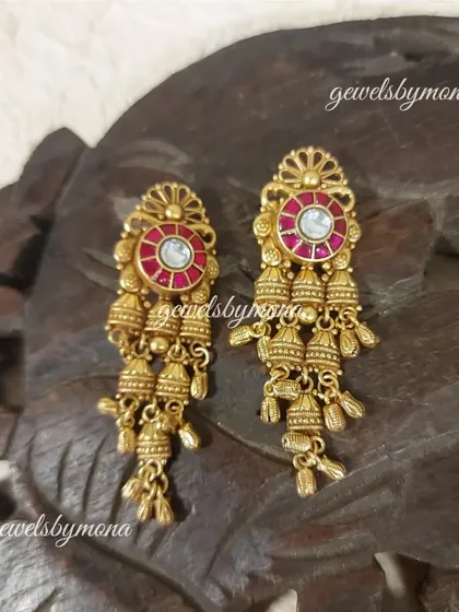 Another beautiful example of Dakshinaya jhumki earrings. The ruby-colored center stone is surrounded by delicate gold work and a cascade of tiny bells, perfect for festive wear.