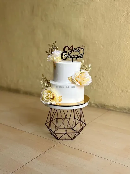 A two-tier engagement cake with white and gold flowers. The design is both modern and timeless, perfect for a stylish celebration.