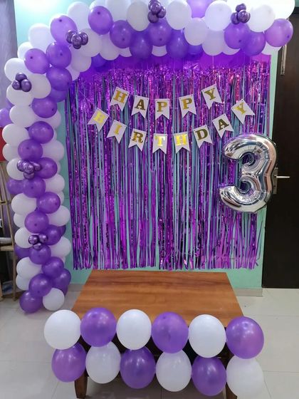 A simple and pretty half-arch in purple and white for a 3rd birthday. The setup includes a shimmer curtain, banner, and number balloon.