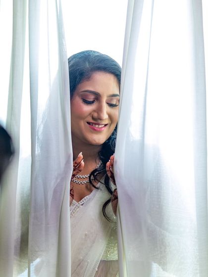 A soft and romantic shot of the bride through a curtain. Her smile and the gentle lighting create a beautiful, ethereal mood.