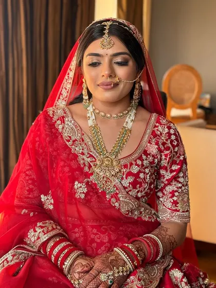 A portrait of a 'Maharani' bride. Her soft smile and elegant posture are complemented by a classic red bridal look with beautiful pearl and emerald jewelry.