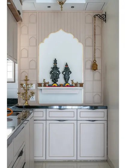 A peaceful and beautifully designed puja nook integrated within the kitchen. The arched design and traditional hanging bell create a serene spiritual corner without disrupting the kitchen's flow.