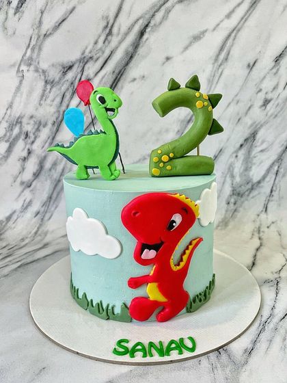 Roar! A dinosaur theme is always a fun challenge. This cake features friendly, hand-modelled fondant dinosaurs and a custom number '2' topper, set against a buttercream sky with fluffy clouds.