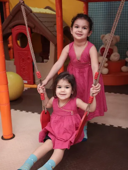 Sisters sharing a moment on one of our indoor swings. Our play area includes a variety of equipment suitable for different ages and energy levels.