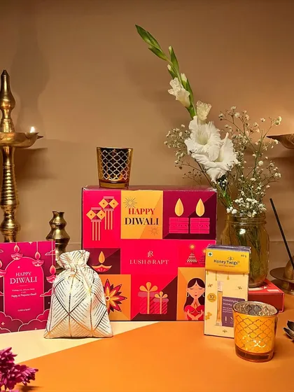A beautifully arranged Diwali hamper featuring traditional diyas, a box of sweets, and fragrant flowers, capturing the true essence of the festival of lights.