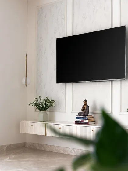 This minimalist floating TV unit in white features grooved drawers and is set against a wall with a subtle floral wallpaper and classic beading.