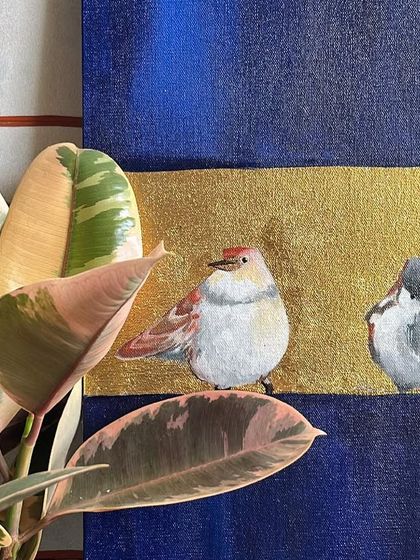 A close-up of a painting featuring small, charming sparrows on a gold leaf band. The piece is styled with a variegated rubber plant, highlighting the connection between my art and nature.