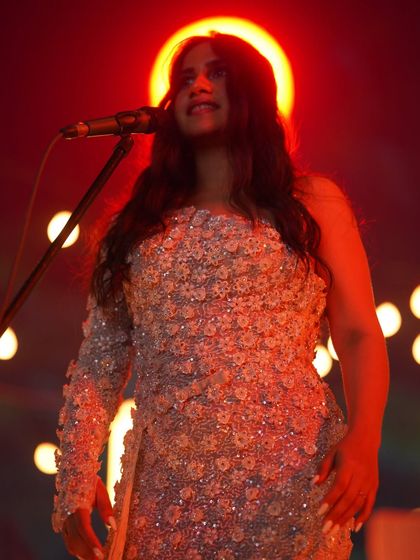 A dramatic, red-lit shot of Nikhita Gandhi, where the detailed texture of the gown I styled for her is beautifully highlighted.