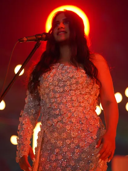 A dramatic, red-lit shot of Nikhita Gandhi, where the detailed texture of the gown I styled for her is beautifully highlighted.