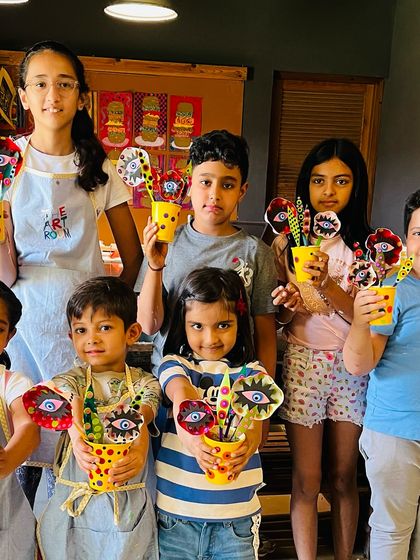 Students hold up the whimsical flower sculptures they created using mixed media, including clay pots and painted elements.