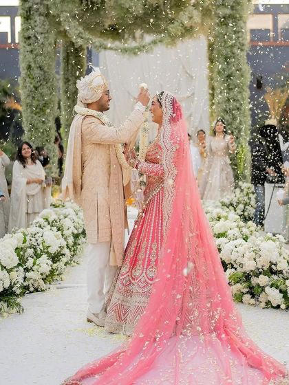 A magical moment under the green floral mandap as the couple exchanges varmalas amidst a shower of white petals. This is what pure happiness looks like.
