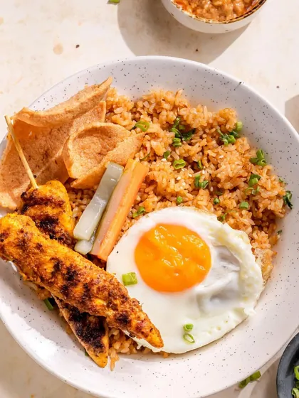 A complete Indonesian Nasi Goreng experience on a plate. This dish features fragrant fried rice, perfectly grilled chicken satay skewers, a sunny-side-up egg, and crispy prawn crackers, served with our secret recipe sauces.