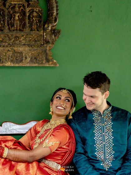 A cross-cultural couple sits on a bench, sharing a look of love, with a traditional bronze sculpture in the background.
