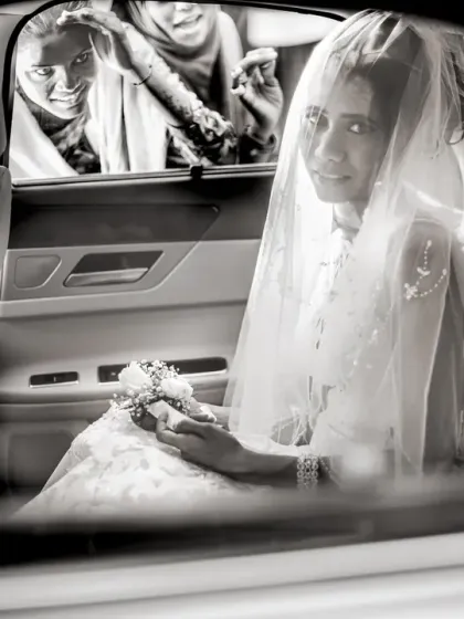 A candid black and white photo of the bride in her car, with a family member peeking in with a smile.