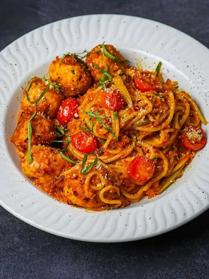 A plate of spaghetti with chicken meatballs in a rich tomato sauce. The dark, textured background gives this classic Italian dish a rustic and authentic feel.